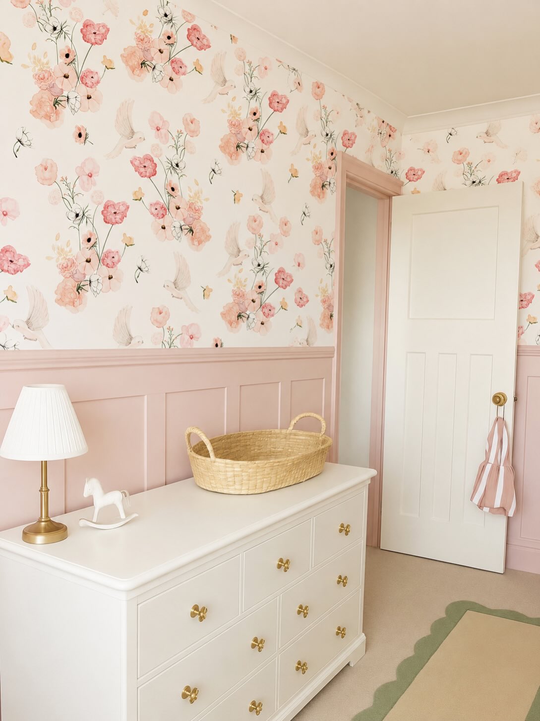 Girls’ bedroom featuring soft floral wallpaper, blush pink wall panelling, white dresser and neutral décor.